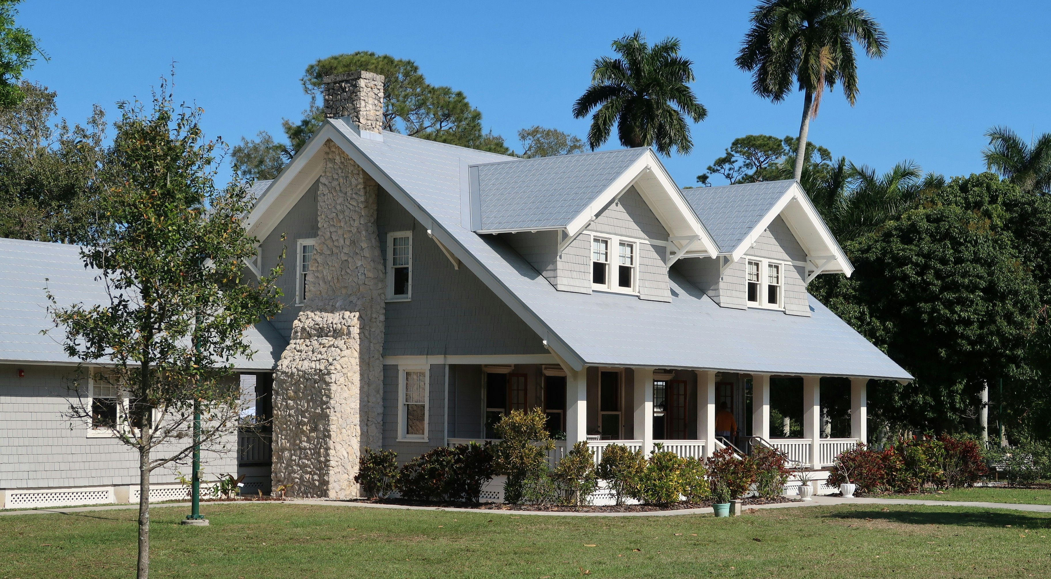 Craftsman-style home with a stone chimney, gray exterior, white trim, and front porch, surrounded by trees and lawn.