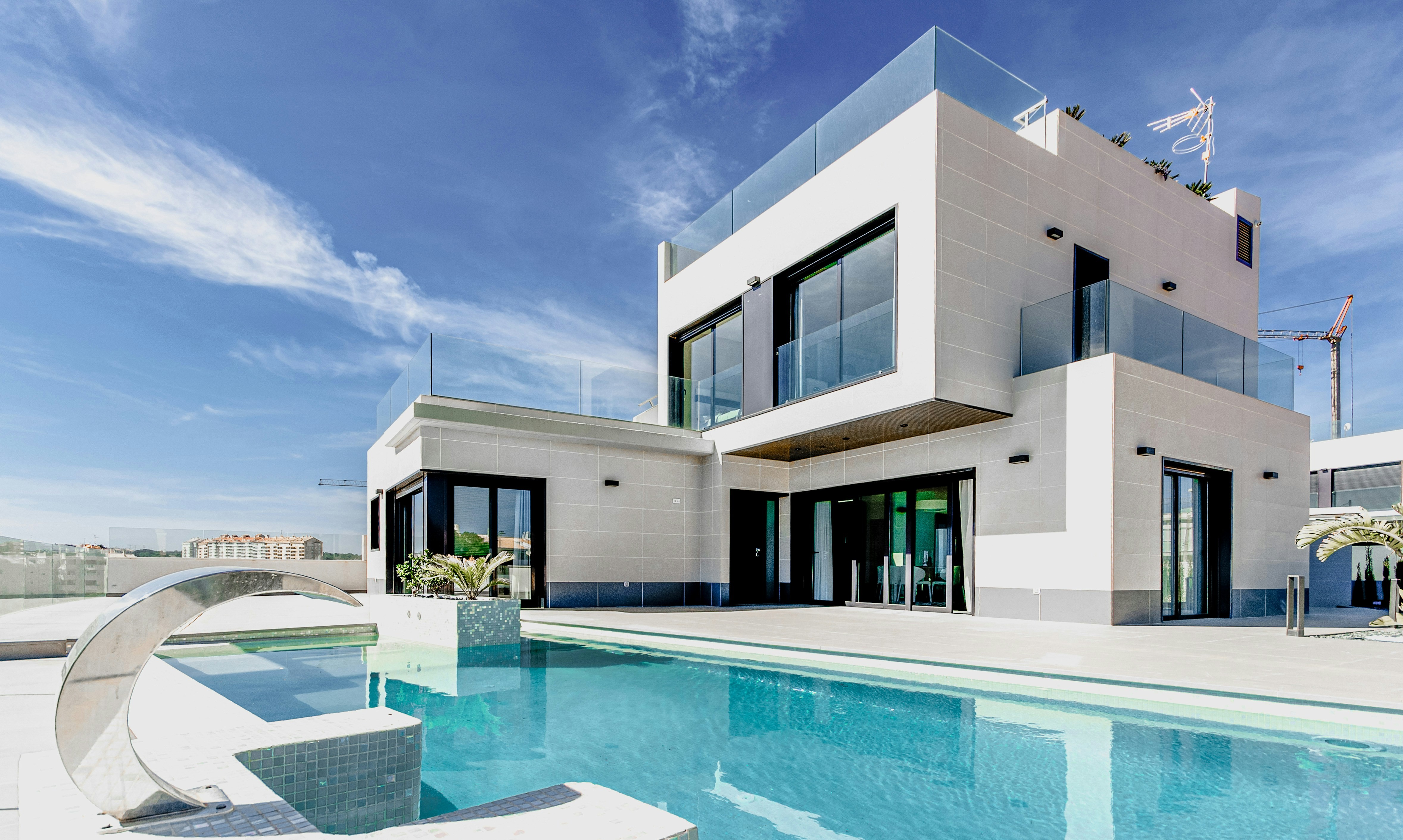 Contemporary two-story luxury home with pool, large windows, and rooftop terrace under a blue sky.