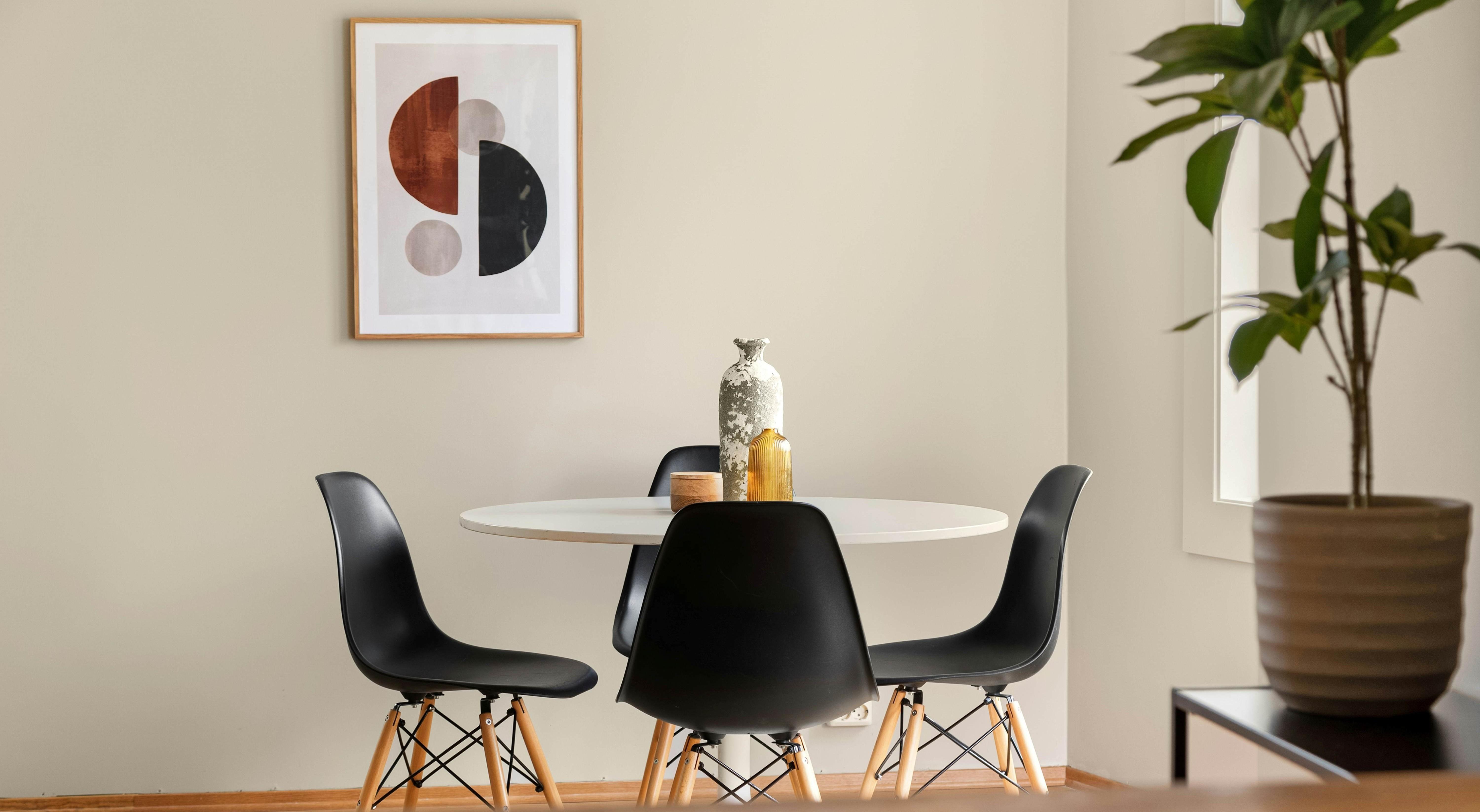 Contemporary dining area with a white round table, black scoop chairs, geometric wall art, decorative vases, and a potted plant - ideal for highlighting lifestyle possibilities with bank statement loans.